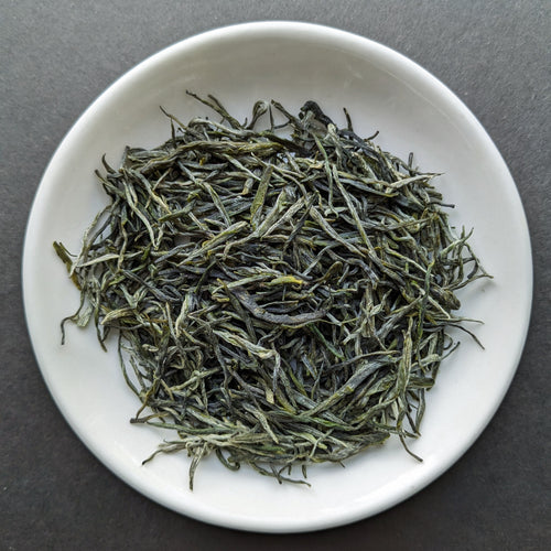 A white porcelain dish filled with wispy dark green tea leaves