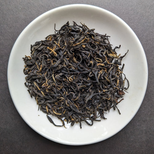 Leaves from black tea in a white porcelain dish. The tea depicted looks to be about 75$ dark brown leaf, adn 25% golden buds