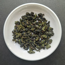 Huang Dan unroasted oolong tea in a white porcelain dish. The tea is green and rolled into tiny balls. 