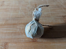 A ball of tea, wrapped in paper which is tied with a tan thread. There is Chinese writing on the paper wrapper, and it is resting on a clean bamboo cutting board.