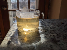 Da Wu Ye Dancong oolong tea, brewed, in a glass with the sun lighting it from behind. The brewed tea is a pale yellow color