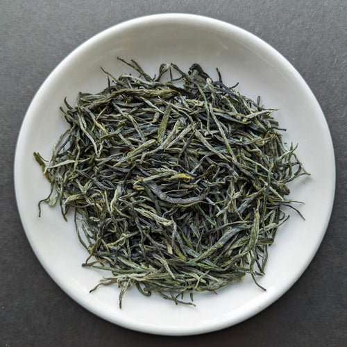 A white porcelain dish filled with wispy dark green tea leaves 