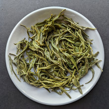 A white porcelain dish filled with long, thin, brewed green tea leaves