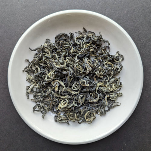 Premium Hui Long green tea, unbrewed, on a small white porcelain dish 