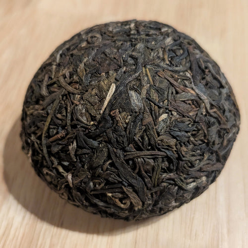 A 100g puerh tuo, unwrapped, on a tabletop. its color is a very dark brown verging on black