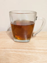 Yi Mei Ren Black Tea in a glass mug. The tea liquor is a clear golden brown.