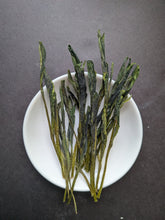 Long, flattened, green tea leaves on a small white dish against a dark grey background